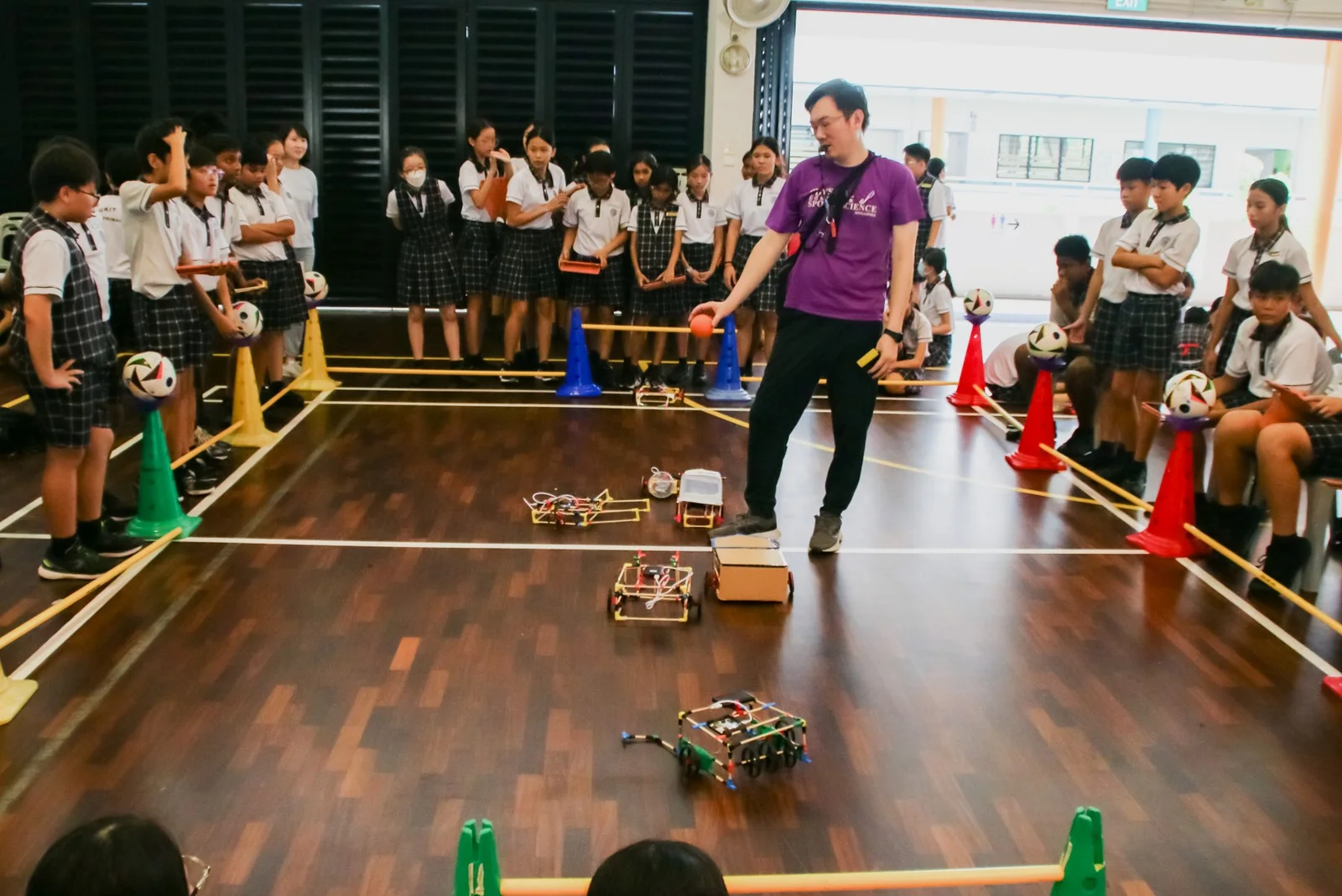 A school hall, a teacher demonstrating, robots and cones on the floor