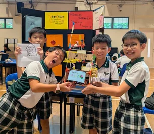 Students in uniform at a table with a laptop and the robot they built